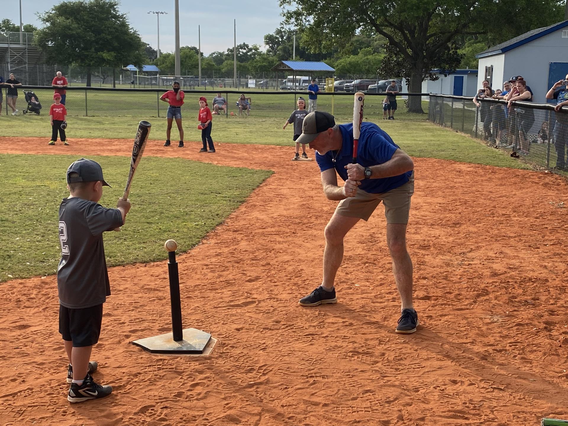 Man holding a baseball bat showing a child how to swing a bat.