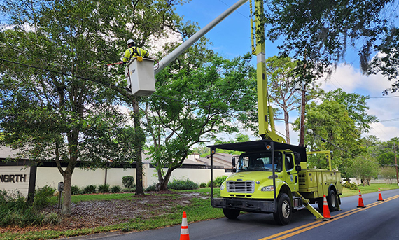 OEU employee in a bucket truck trims trees by the road